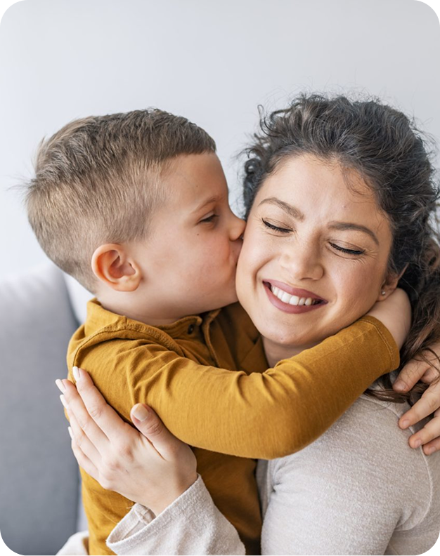 Criança abraçando e beijando o rosto da mãe, ambas sorrindo.